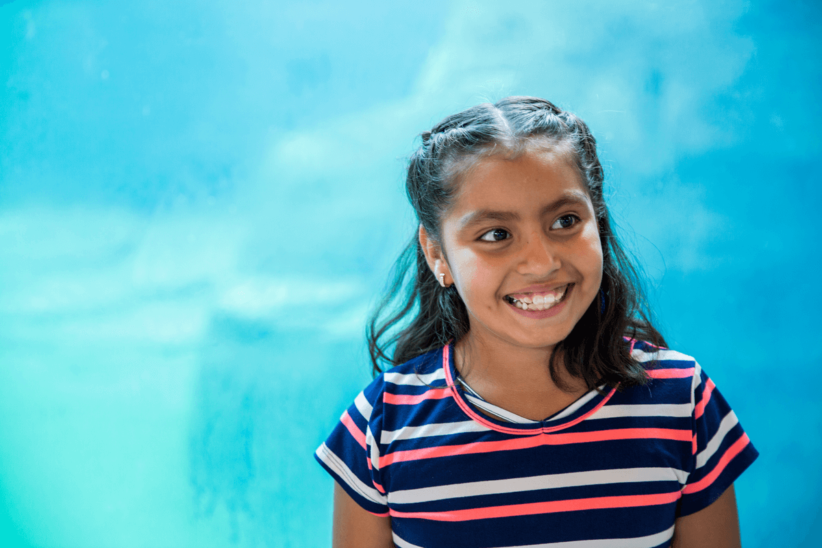 Child at aquarium smiling standing in front of glass